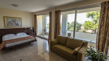 A hotel room with a bed, a sofa, a large window, and a painting on the wall.