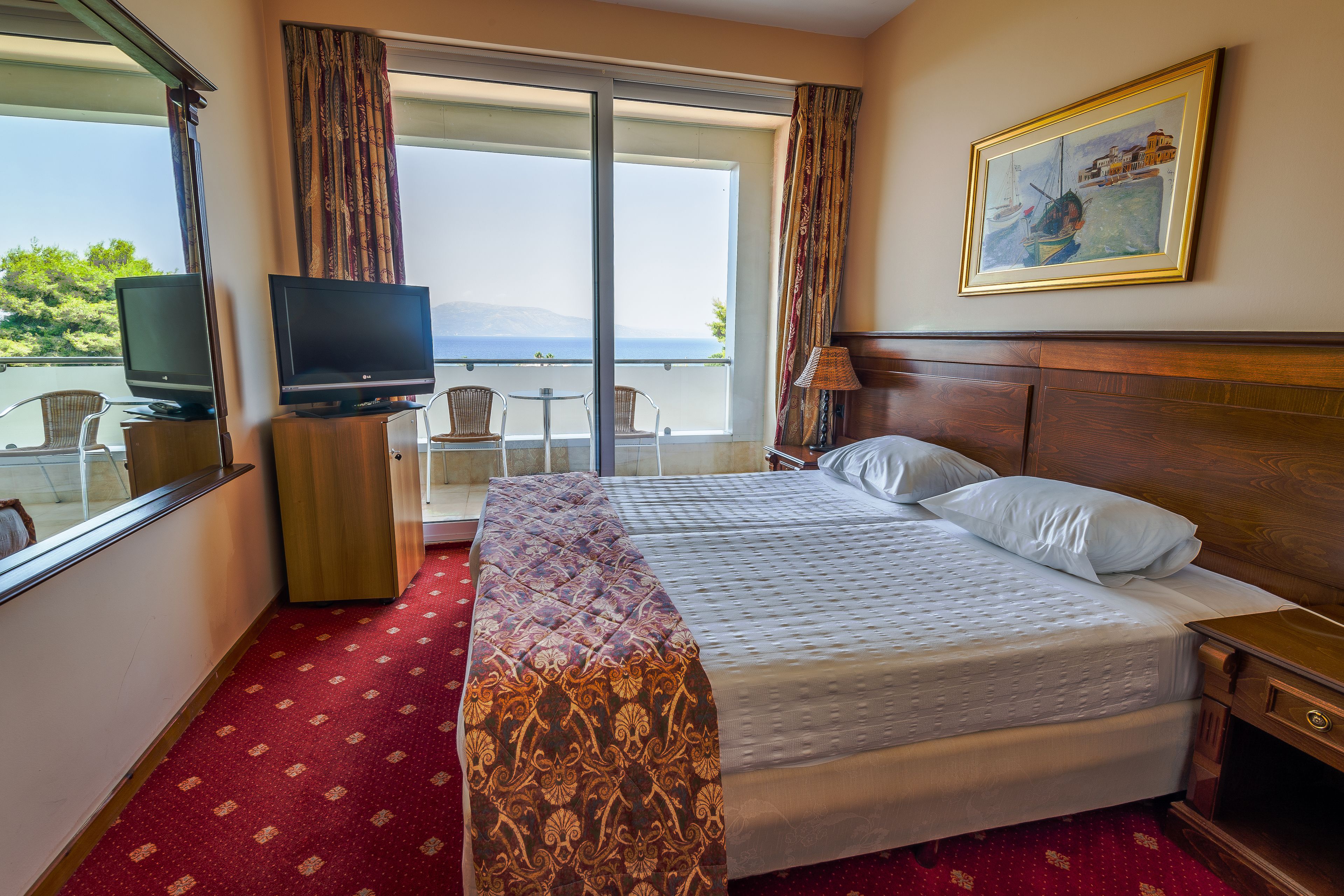 A hotel room with a bed, a television, a desk with chairs, and a window with curtains.