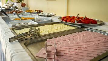 Un bufé con distintos alimentos, como jamón en rodajas, queso y tomates.