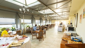 A spacious dining area with high ceilings and large windows, tables set with plates, cutlery, and bread.