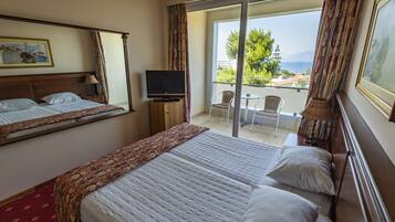 A hotel room with a large bed, a television on a small table, a balcony with a chair, and a view of the sea.