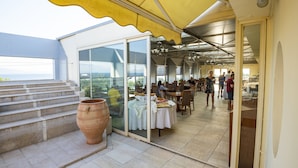A restaurant with outdoor seating, a large window, and a view of the sea.