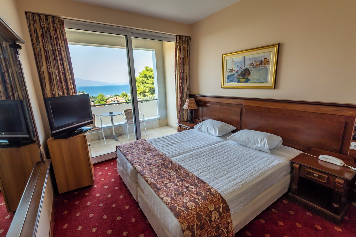 Une chambre d’hôtel avec un grand lit, une télévision, un bureau avec une lampe et un balcon donnant sur la mer.