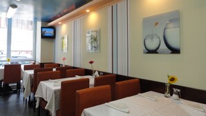 A restaurant with tables set for dining, a TV mounted on the wall, and artwork on the walls. - Relax Comfort Suites (Bucharest)
