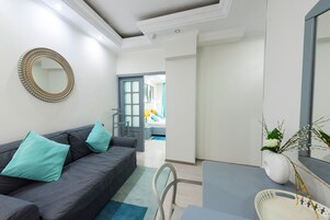Una sala de estar moderna con un sofá gris, cojines turquesa, un espejo redondo y un florero blanco con plantas.