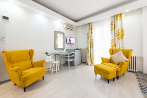 Una sala de estar moderna con dos sillones amarillos, una mesita blanca y un televisor montado en la pared.