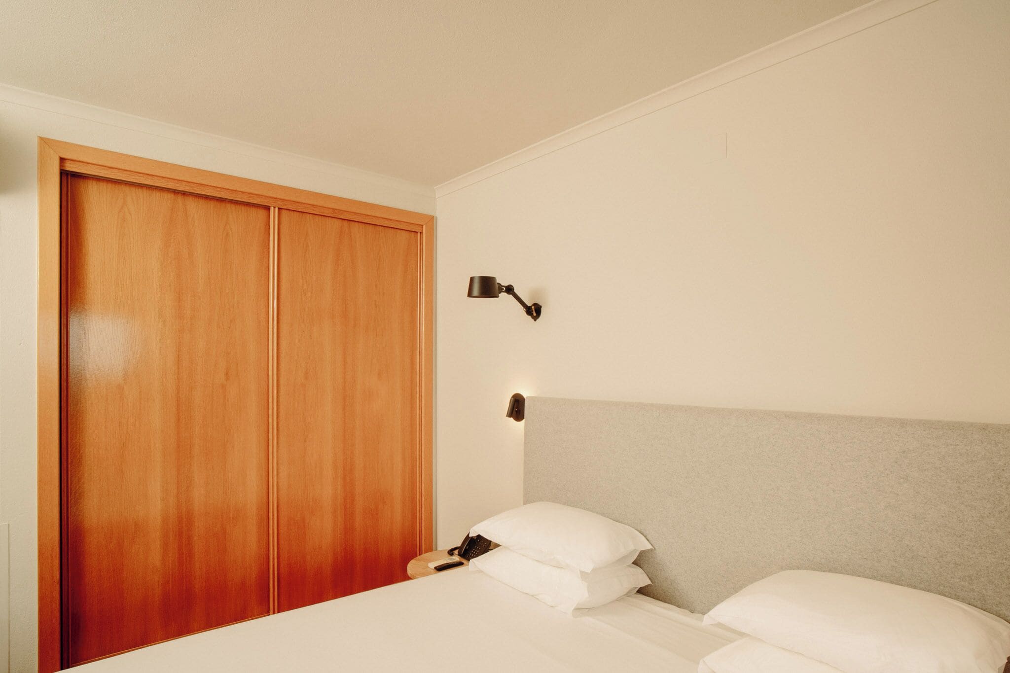 A bedroom with a bed, pillows, a bedside table with a lamp, and a wooden wardrobe.