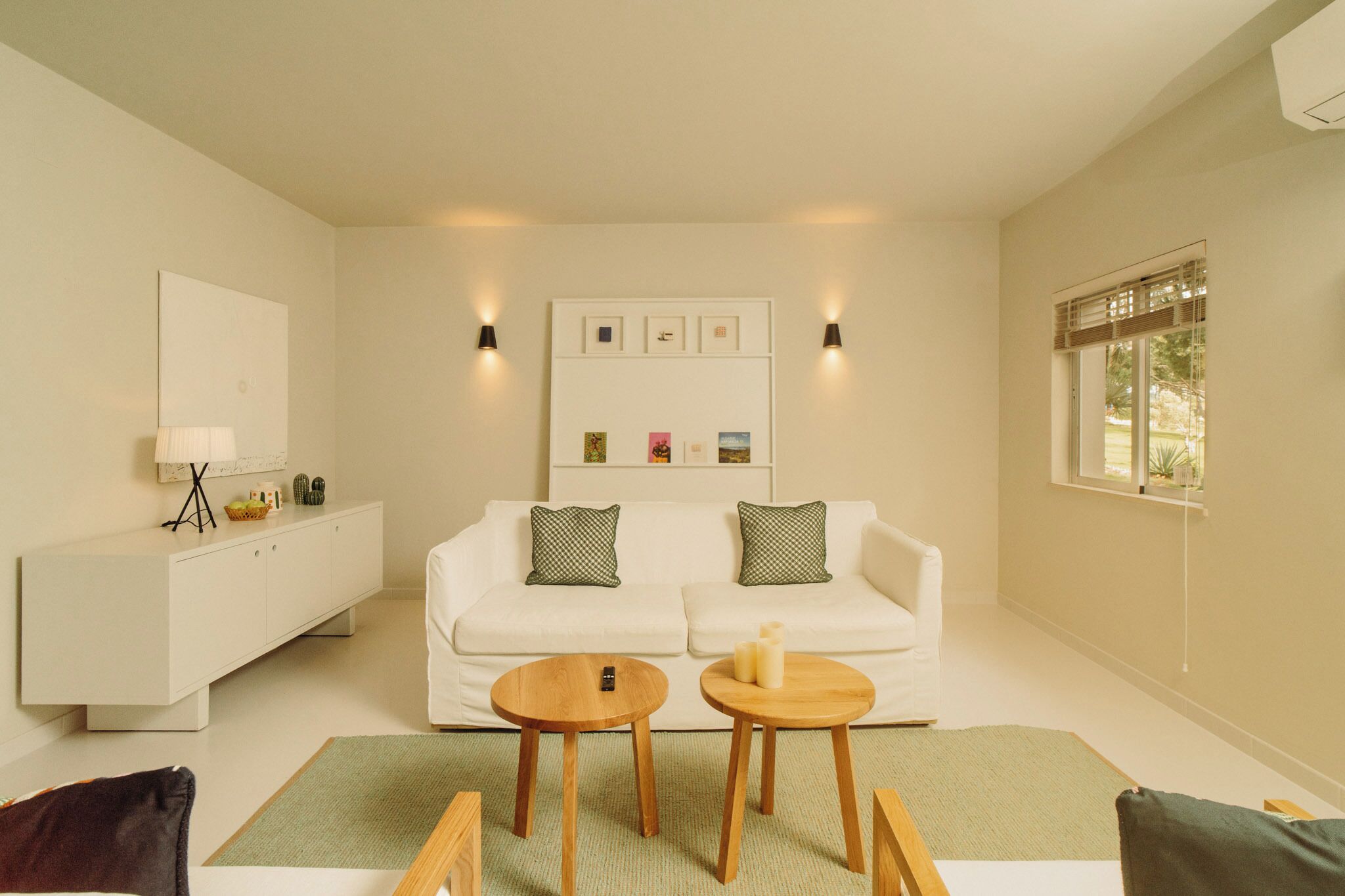 A modern living room with a white sofa, two side tables, a white cabinet, and a framed picture collection on the wall.