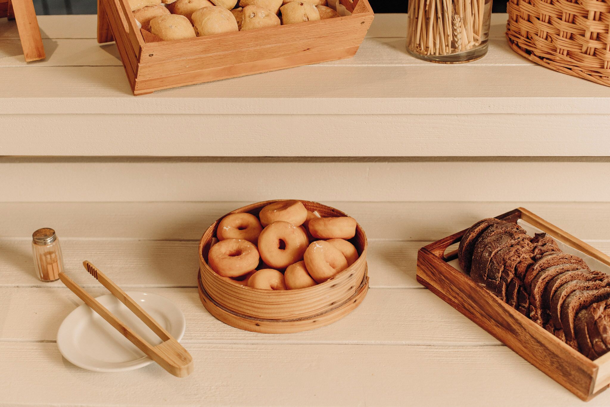 A wooden tray with donuts, a bowl of donuts, and a loaf of bread on a wooden table.