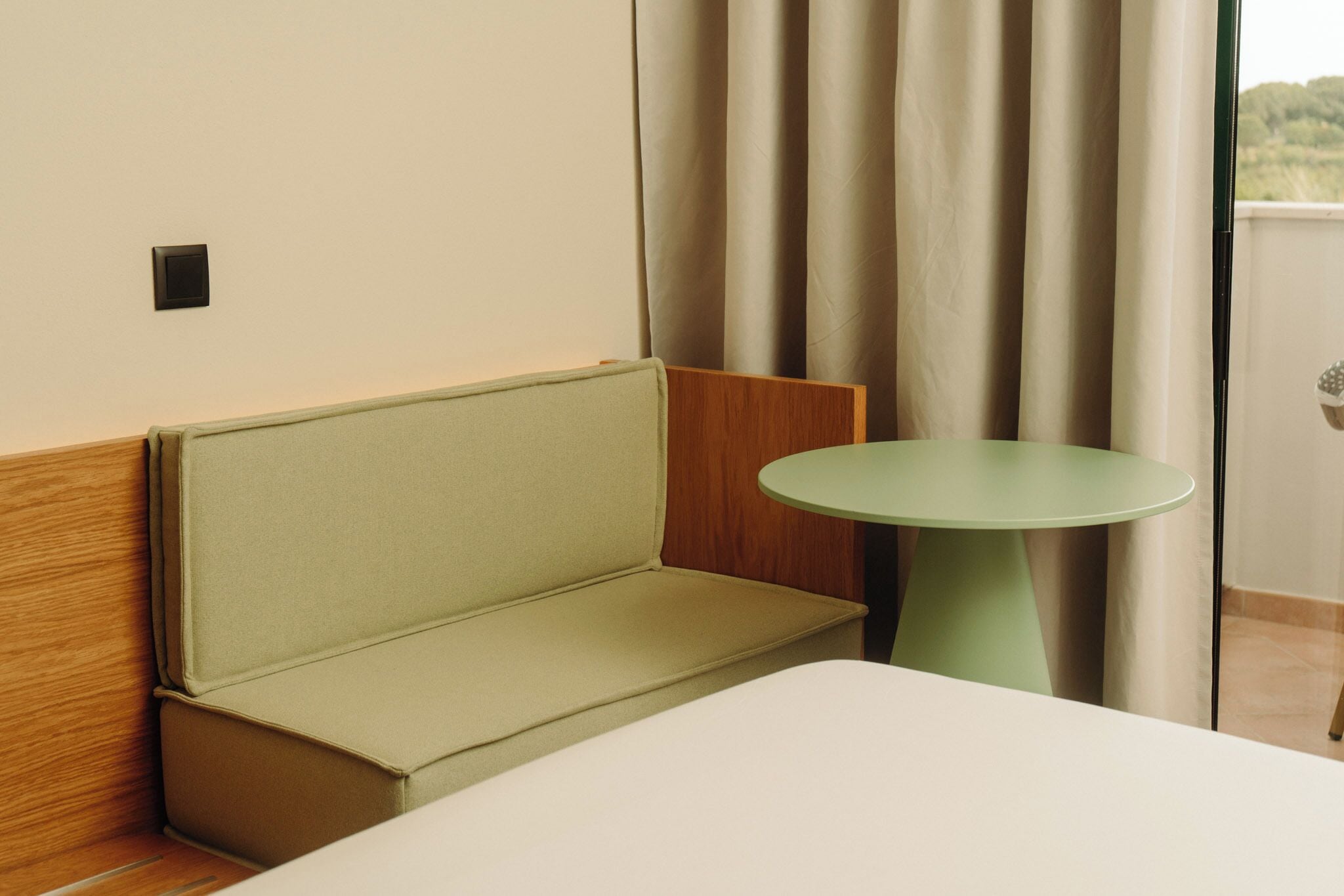 Una habitación con un sofá, una mesita redonda y un ventanal con cortinas.
