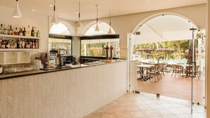 Zona de bar con suelo de baldosas en patrón espiga, una máquina de café y una variedad de botellas y vasos.