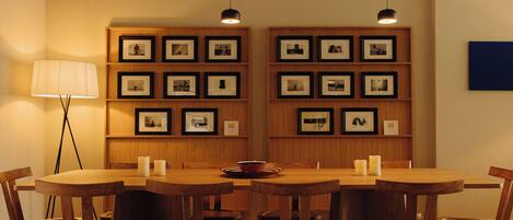 A dining area with wooden tables and chairs, framed pictures on the walls, and a floor lamp.