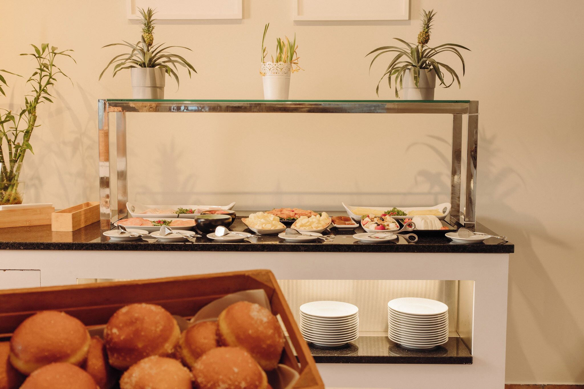 A buffet counter with various food items, a glass display case, and potted plants.