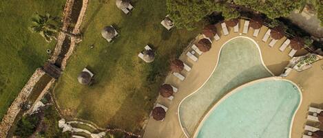 Vista aérea de un complejo turístico con piscina, sillas de descanso y palmeras.