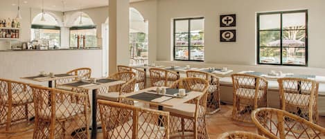 A restaurant with wicker furniture, a bar area, and large windows with views.