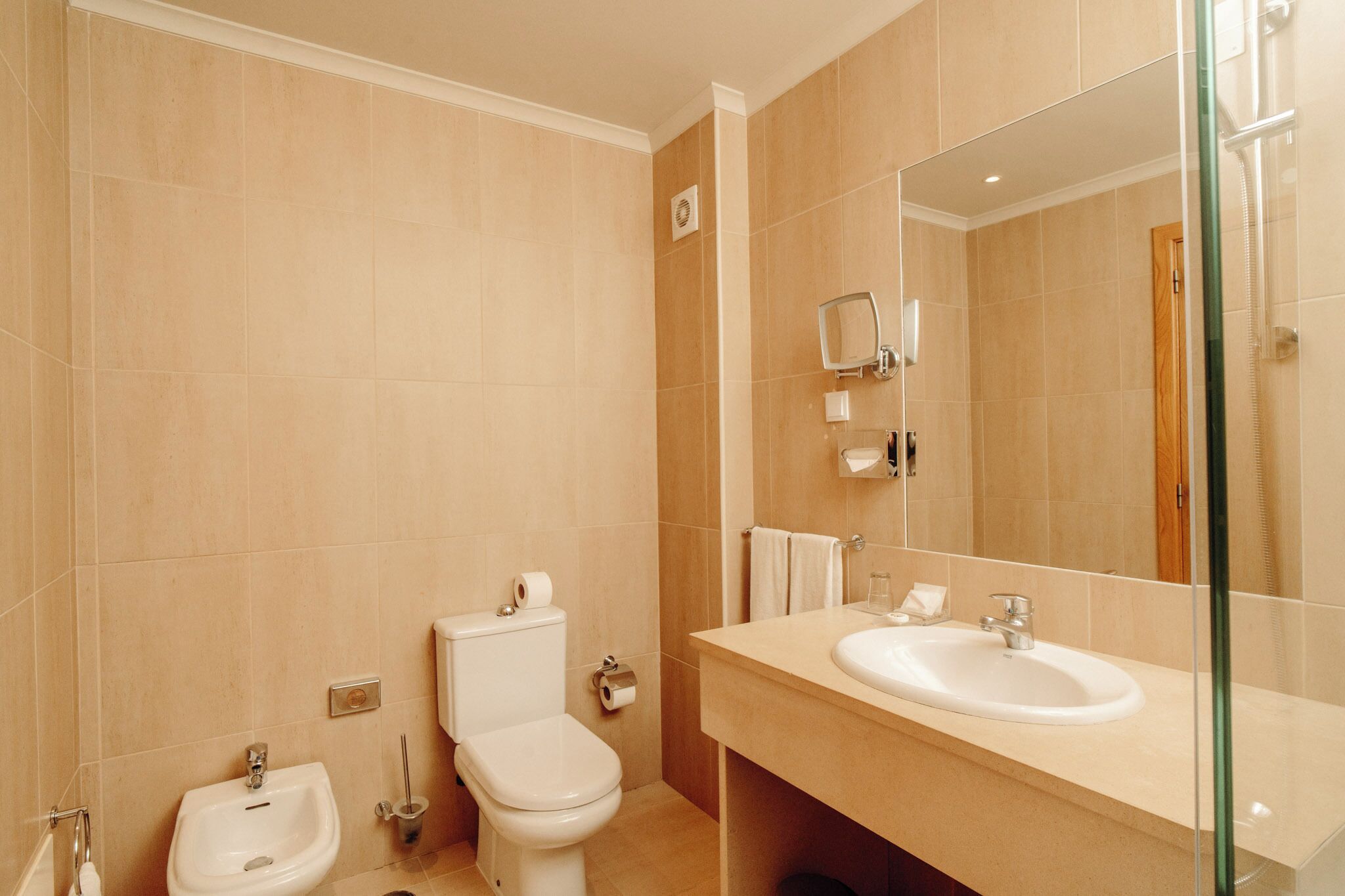 Un baño moderno con bidé, inodoro, lavamanos y un espejo grande.