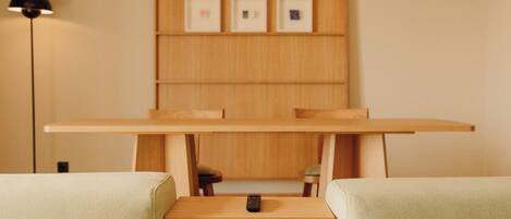 A minimalist room with a wooden table, two cushioned chairs, a remote control on the table, and framed pictures on the wall.
