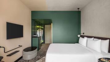 Una habitación de hotel moderna con una cama grande, un televisor de pantalla plana, una zona de estar pequeña y un armario con espejo.