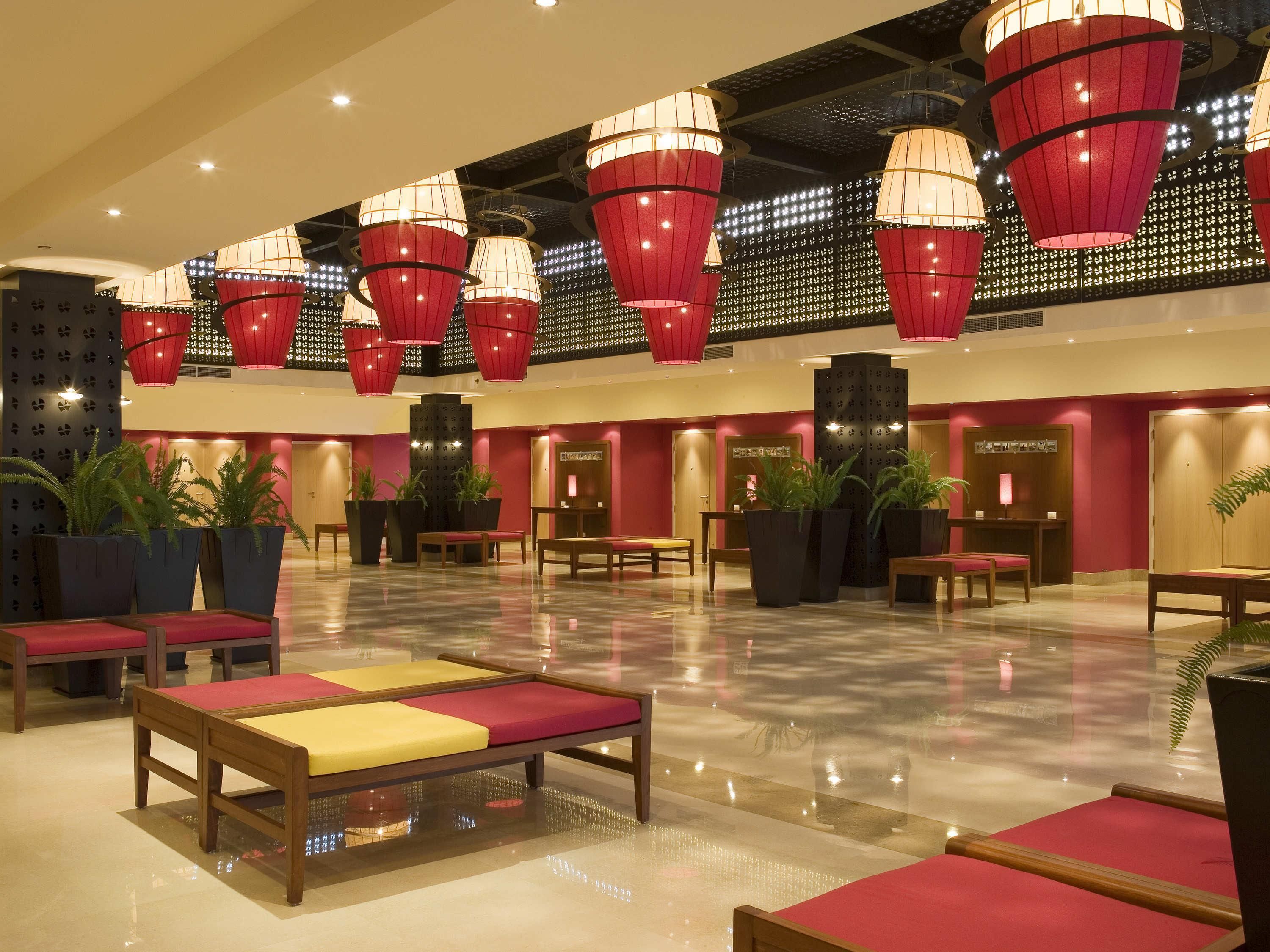 A spacious lobby with multiple seating areas, a reception desk, and decorative red hanging lamps.