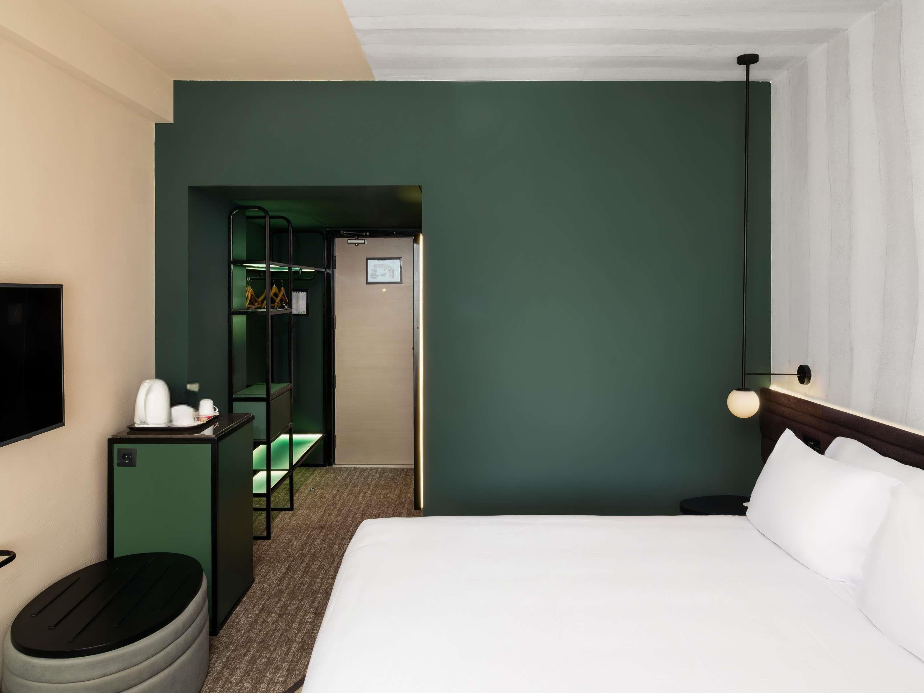 Una habitación de hotel con cama, televisión, escritorio con hervidor, cesto de basura y armario.