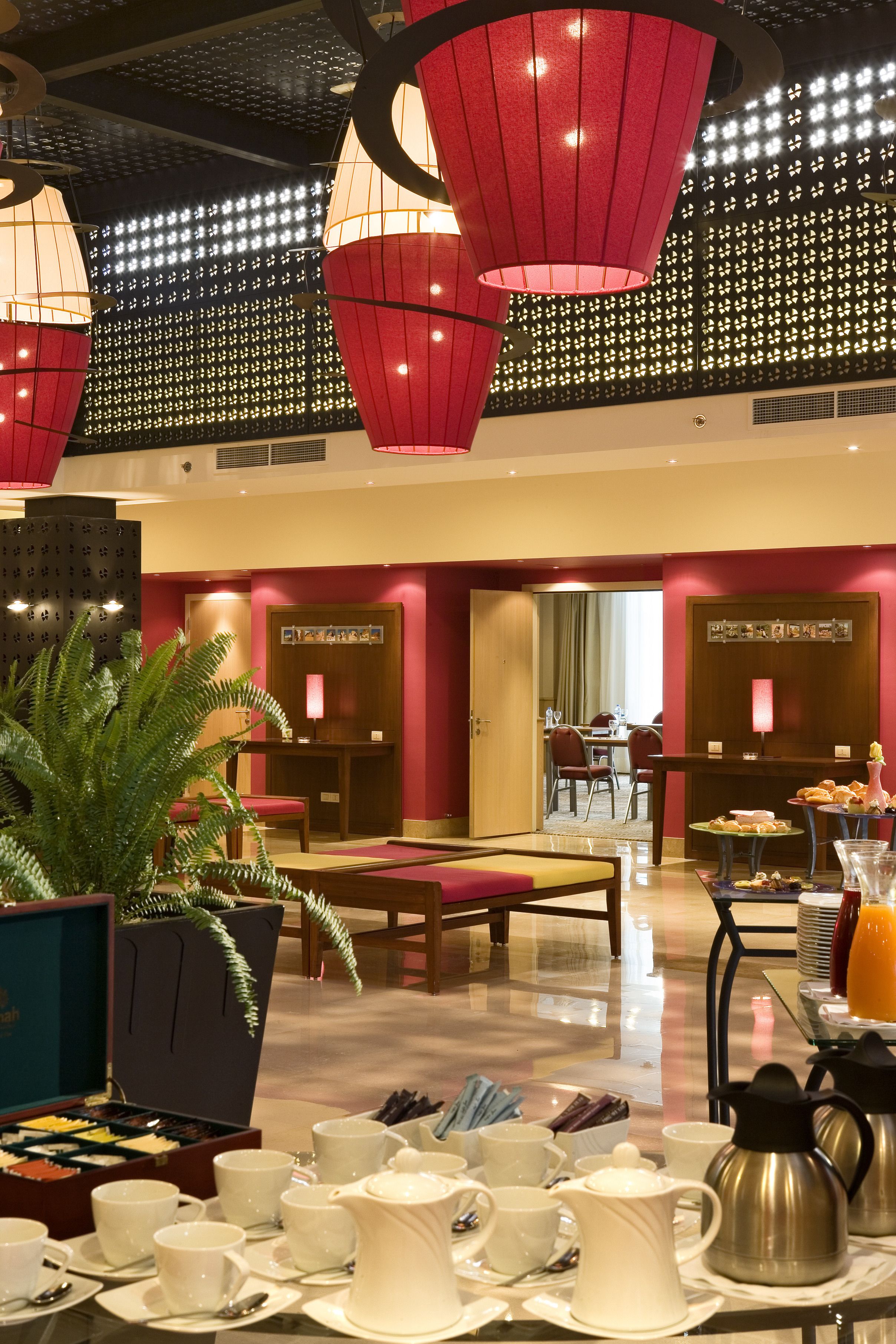 Un vestíbulo de hotel con zona de comedor, mostrador de recepción y una planta grande en maceta.