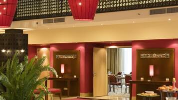 Un vestíbulo de hotel con zona de comedor, mostrador de recepción y una planta grande en maceta.