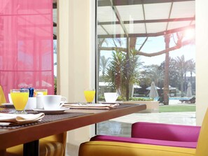 A breakfast table with orange juice, a cup, and a plate, overlooking a pool and palm trees. - Novotel Cairo 6th Of October (6th of October City)