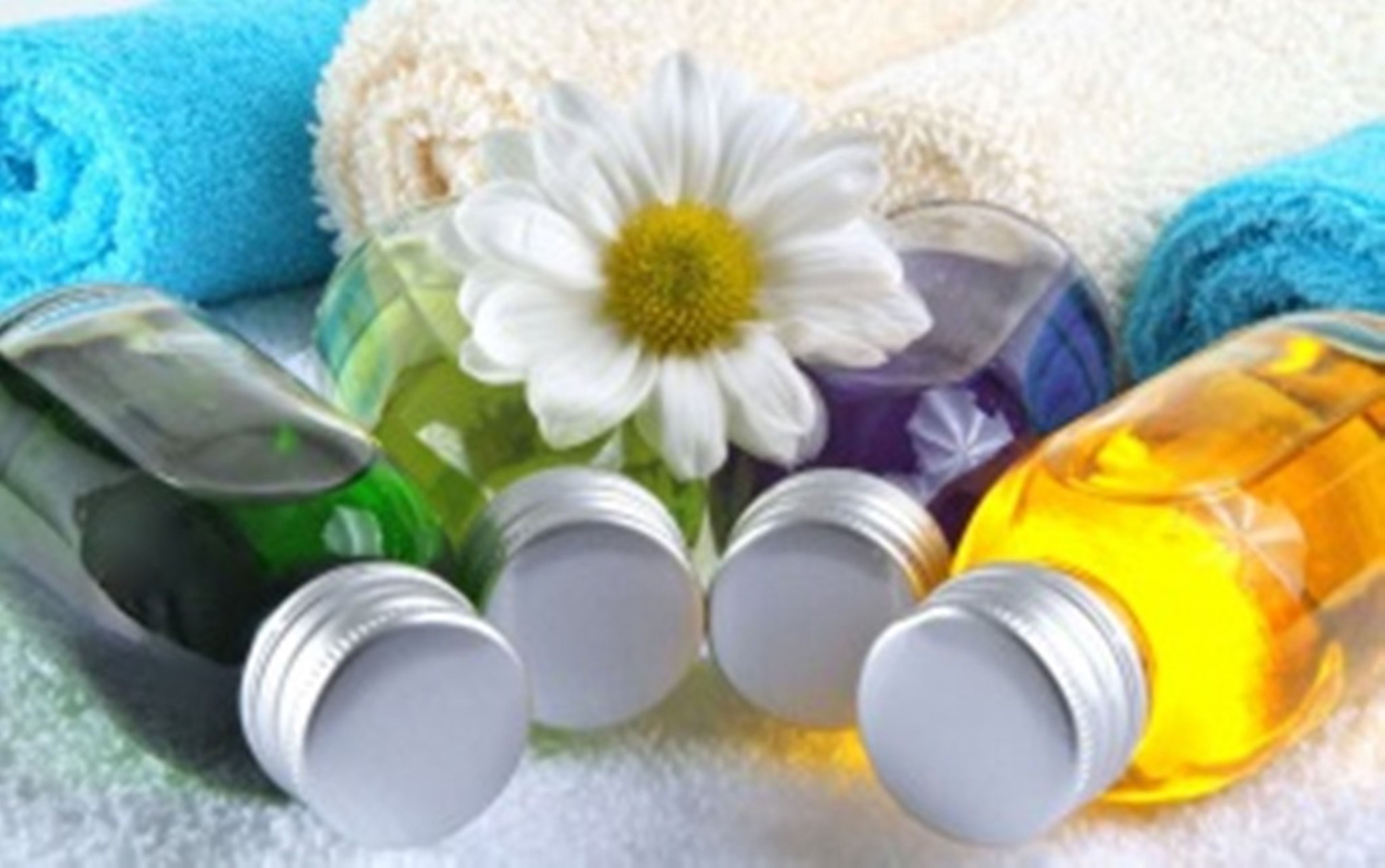A collection of toiletries including a white flower, a green bottle, a purple bottle, and a yellow bottle, all placed on a white surface.