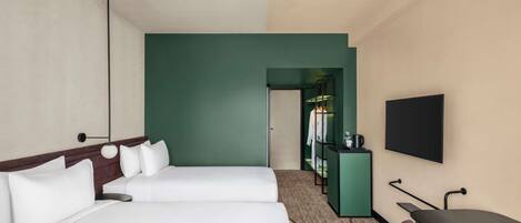 A hotel room with two beds, a TV, a desk, and a kitchenette.