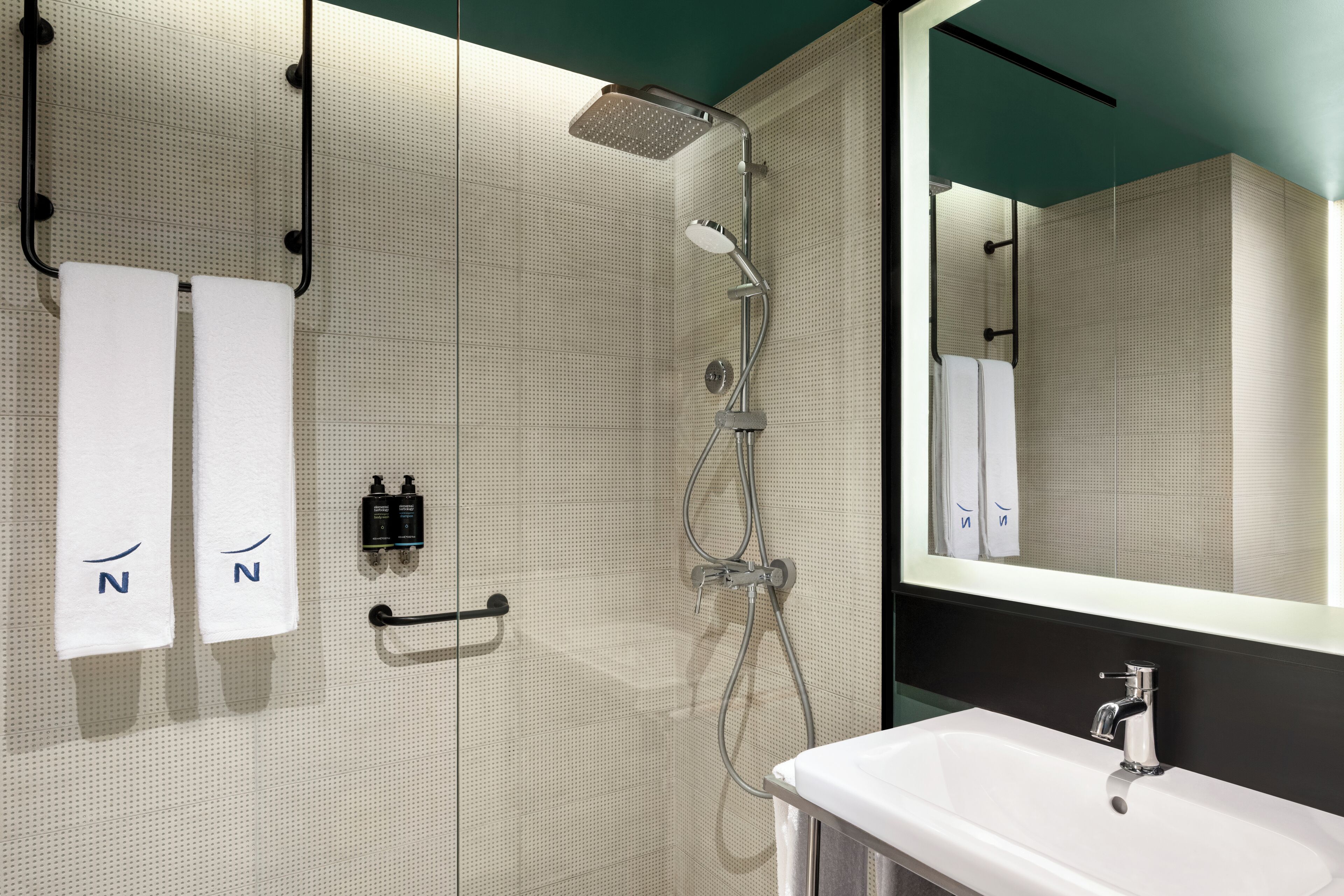 A modern bathroom with a shower, a sink, and two towels hanging on hooks.