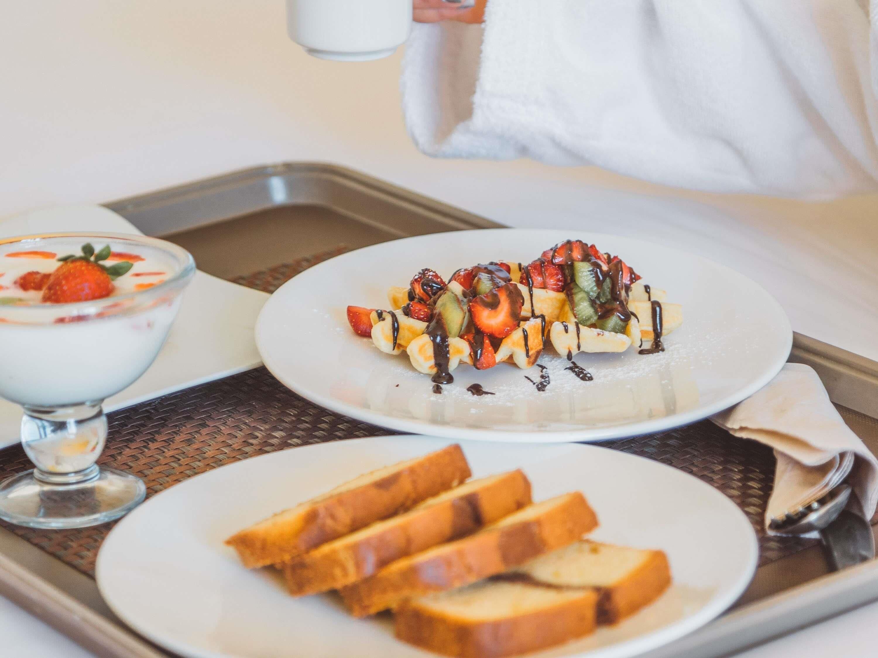 A breakfast tray with a fruit-topped waffle, a glass of yogurt with strawberries, and slices of toast.