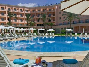 A hotel with a swimming pool, lounge chairs, umbrellas, and palm trees. - Novotel Cairo 6th Of October (6th of October City)