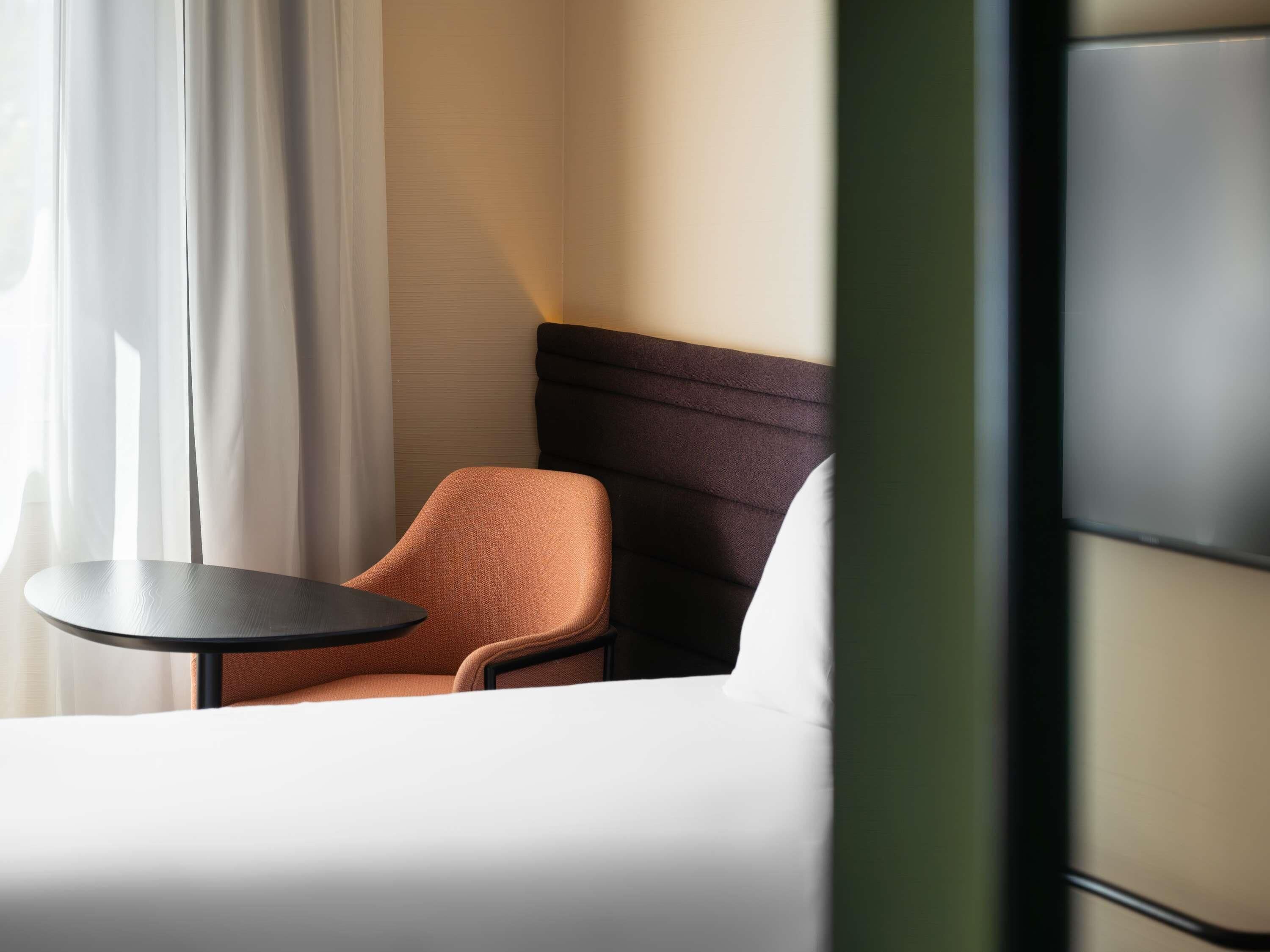 A hotel room with a bed, a small table, a chair, and a headboard.
