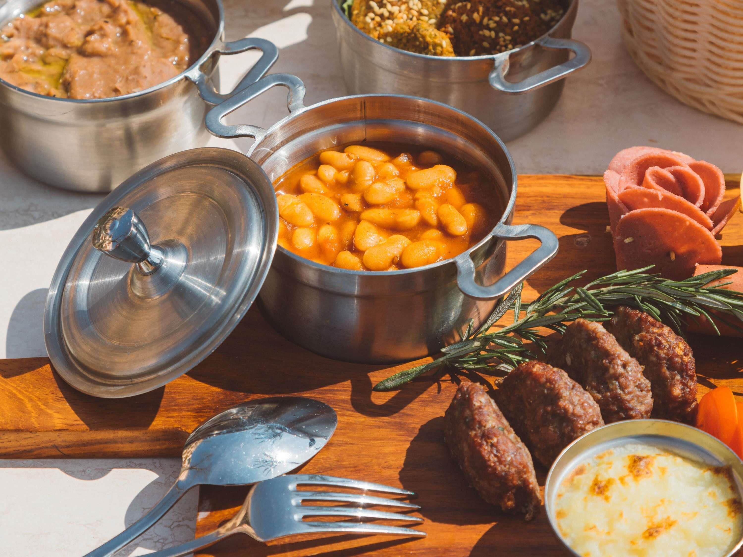 Impostazione di un pasto con un tegame di fagioli, carne a fette, una ciotola di salsa e un tagliere con utensili.