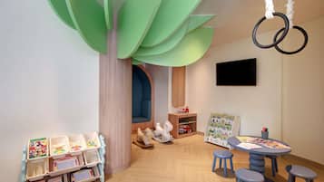 Un cuarto de juegos para niños con una estructura de madera, una mesa con taburetes y una estantería llena de juguetes y libros.