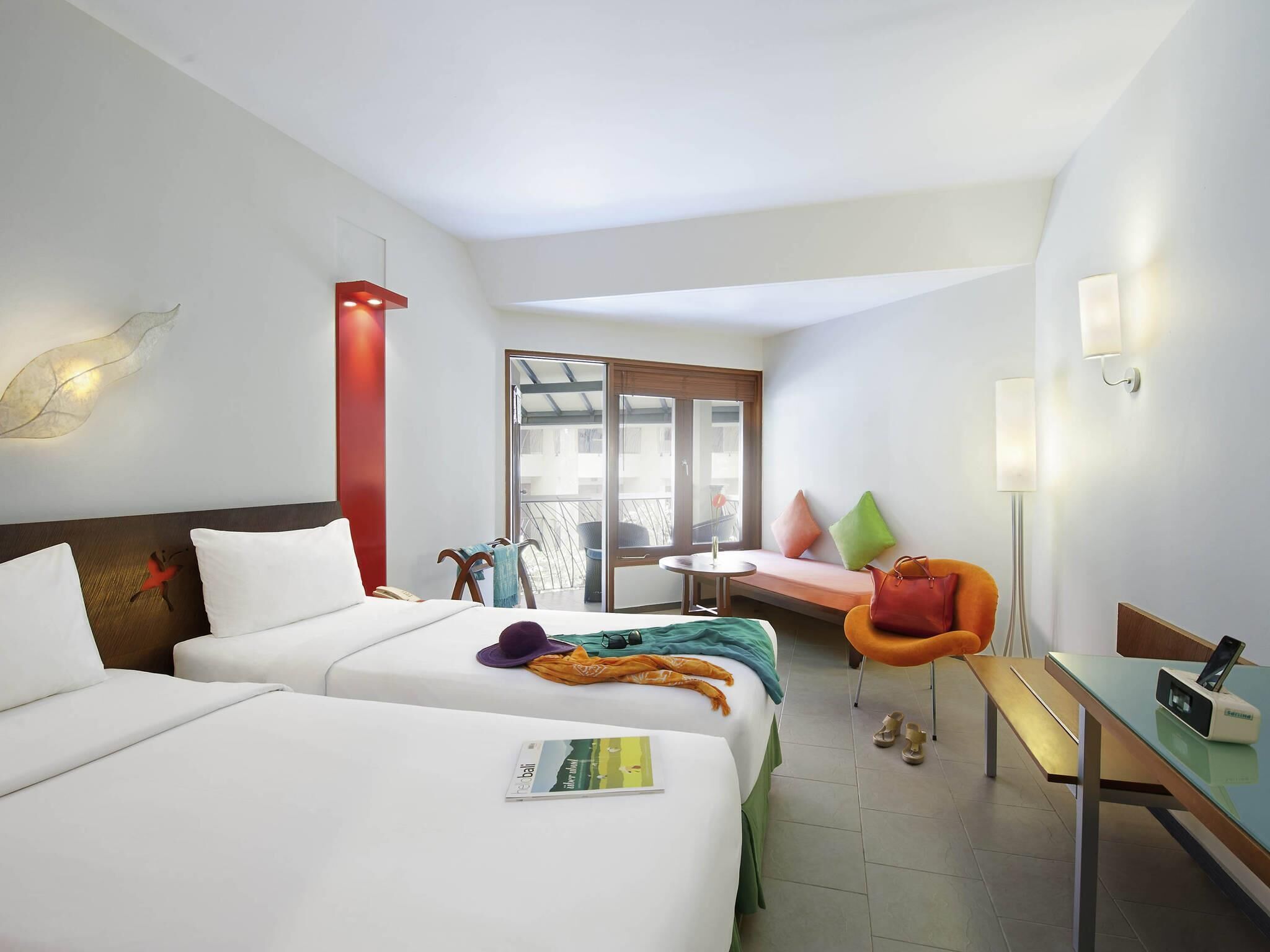A hotel room with two beds, a sofa, a chair, a desk, and a view through a sliding door.