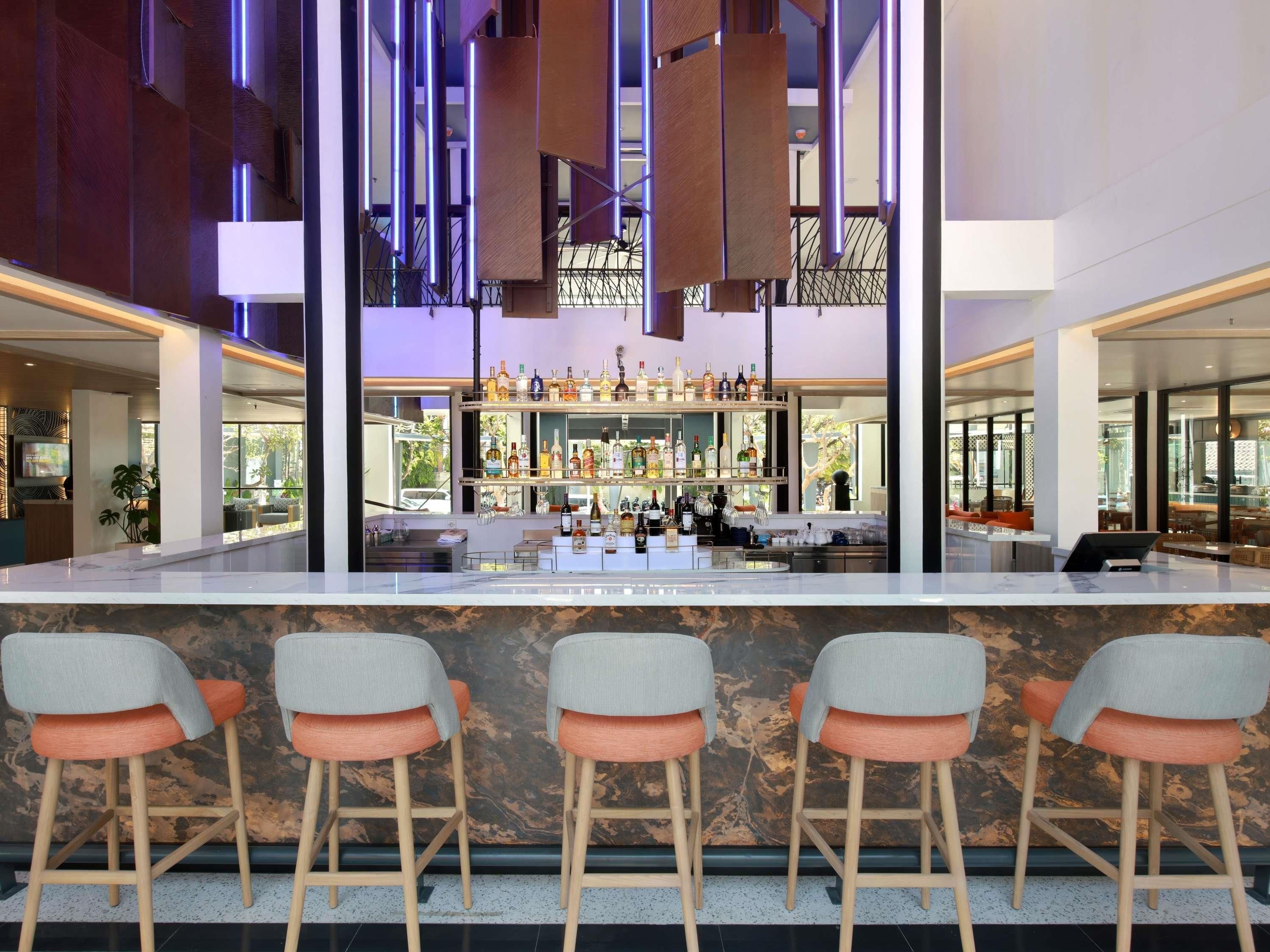 A bar area with a marble countertop, bar stools, and a variety of bottles.