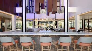 A bar area with a marble countertop, bar stools, and a variety of bottles.