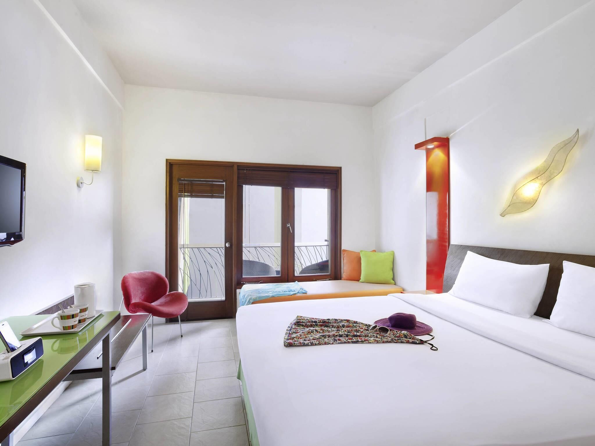 Une chambre d’hôtel avec un lit, un bureau doté d’un téléphone et d’une tasse, une chaise, une télévision et un balcon avec une porte.