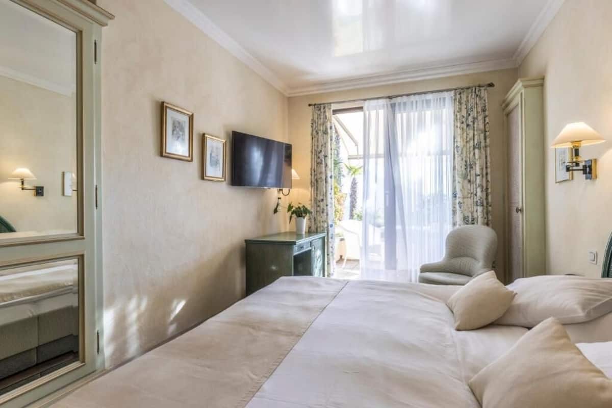 A hotel room with a large bed, a TV mounted on the wall, a desk with a chair, and a view through the window.