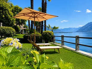 A lakeside garden with a wooden deck, a lounge chair, and an umbrella. - Boutique Hotel La Rocca (Ronco sopra Ascona)