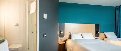 Une chambre d’hôtel équipée d’une douche, de toilettes, d’un lit avec une literie blanche et d’un mur d’accent de couleur turquoise.
