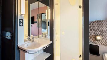 A modern bathroom with a white sink, a large mirror, and a shower area.