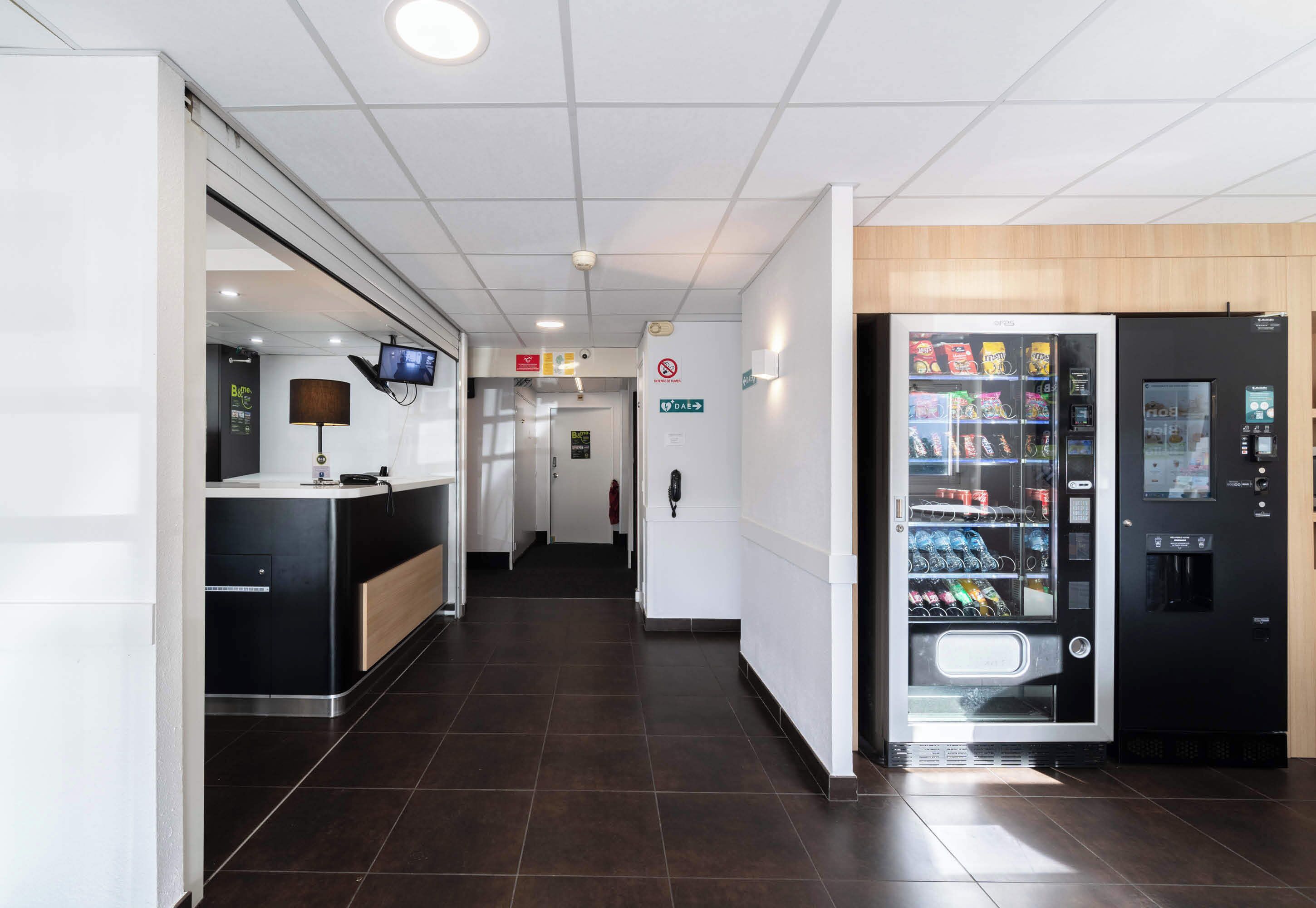 Een hotelhal met een receptiebalie, een automaat en een duidelijke route naar de uitgang.