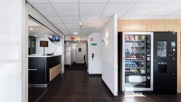 Een hotelhal met een receptiebalie, een automaat en een duidelijke route naar de uitgang.