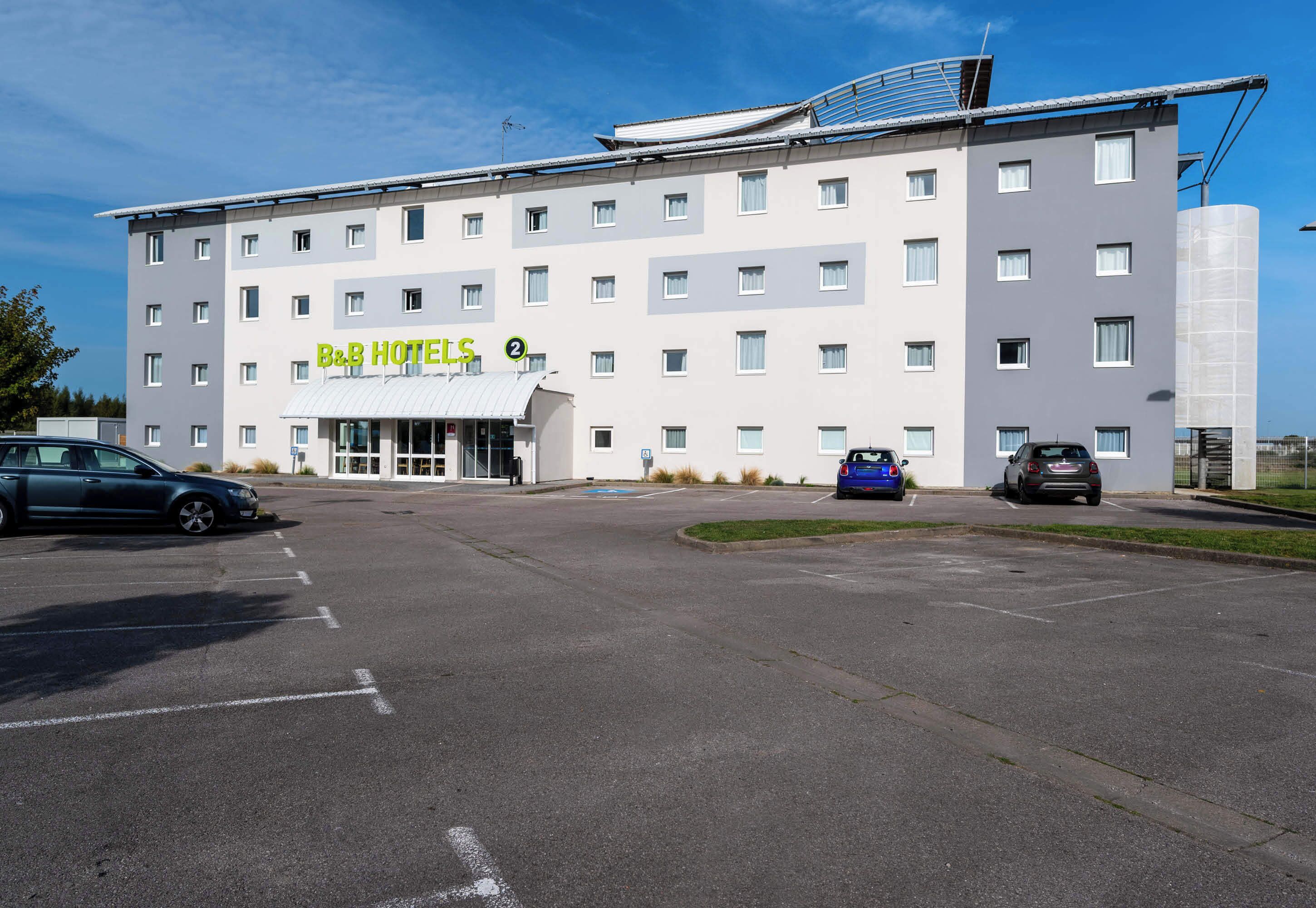 Un hotel B&B con diseño moderno, varios pisos y un estacionamiento con varios coches.
