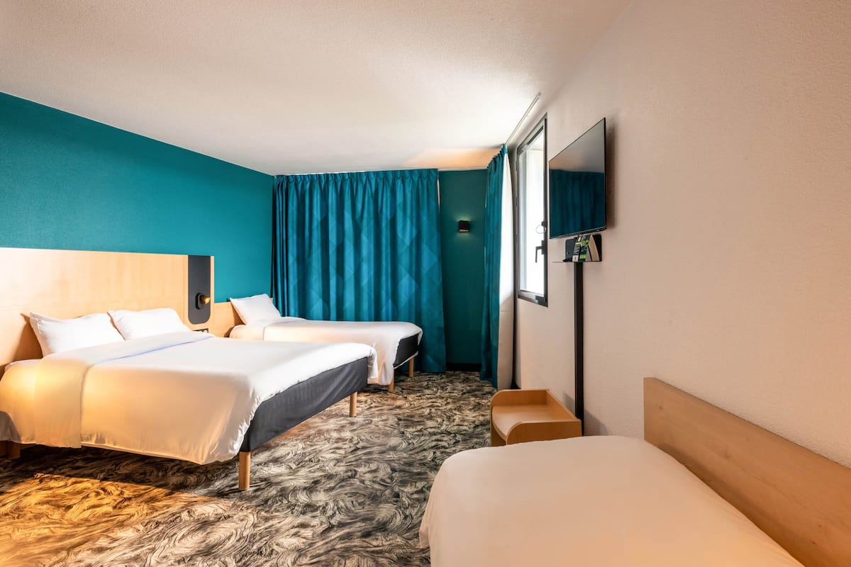 A hotel room with two beds, a flat-screen TV, a wooden headboard, and a teal accent wall.