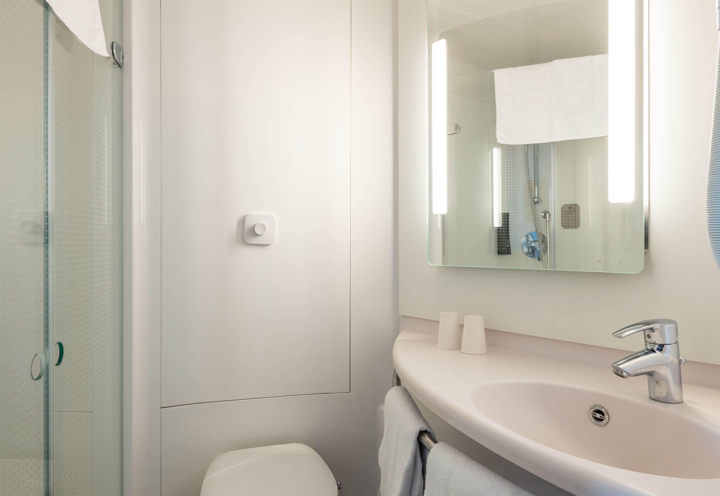 A modern bathroom with a glass shower enclosure, a white sink with a mirror above it, and a toilet.