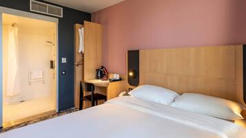 Una habitación de hotel con cama, escritorio, silla, ducha y toallero.