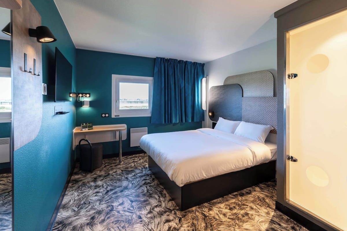 A modern hotel room with a large bed, a desk, and a window with curtains.